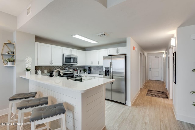 kitchen featuring light wood-type flooring, tasteful backsplash, a kitchen bar, kitchen peninsula, and appliances with stainless steel finishes