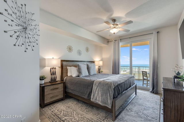 bedroom with a water view, a textured ceiling, access to outside, ceiling fan, and light hardwood / wood-style floors