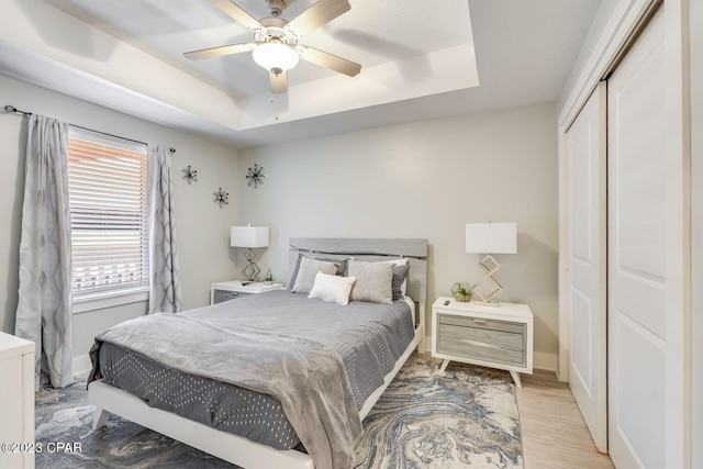 bedroom featuring a raised ceiling, hardwood / wood-style floors, ceiling fan, and a closet