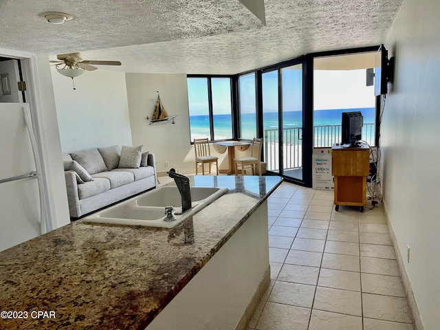 tiled living room with ceiling fan, a wall of windows, sink, a water view, and a textured ceiling