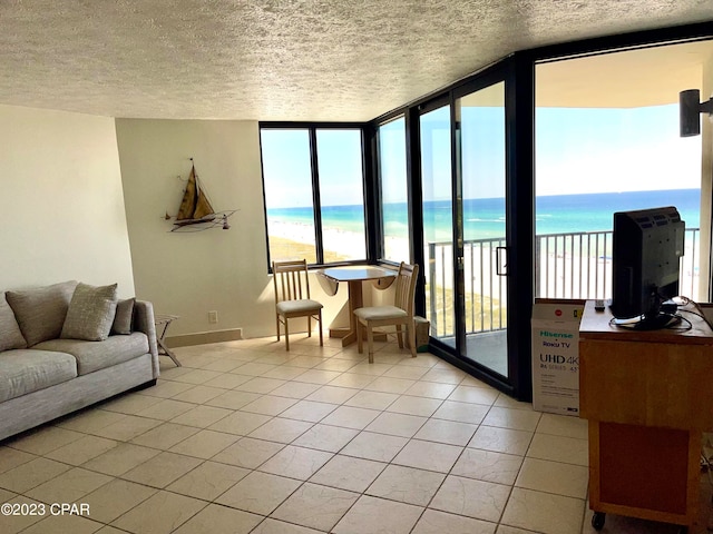 living room featuring a wall of windows, a view of the beach, a water view, light tile floors, and a textured ceiling