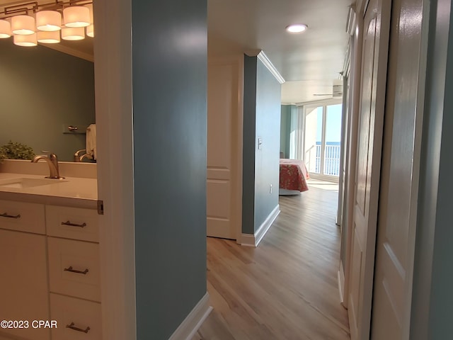 corridor with light wood-type flooring, crown molding, baseboards, and a sink