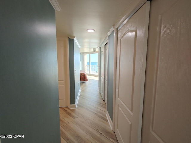 hallway featuring baseboards, crown molding, and light wood finished floors