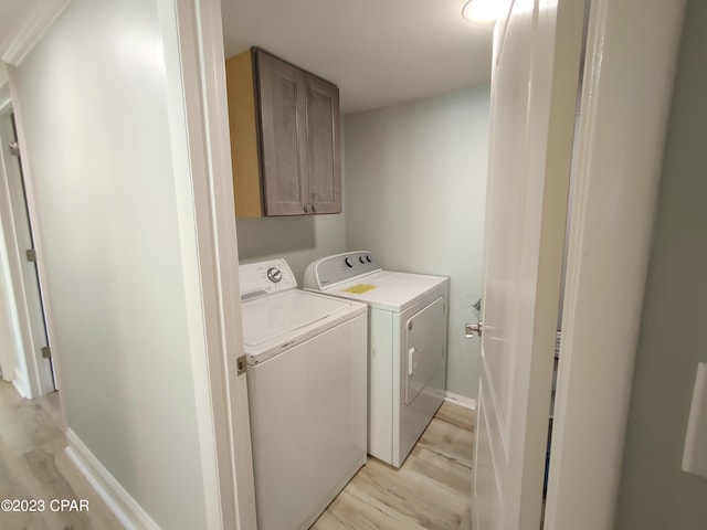 washroom featuring light wood-style floors, baseboards, cabinet space, and washing machine and clothes dryer