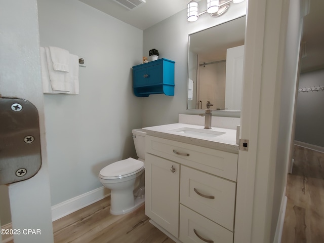 bathroom featuring visible vents, baseboards, toilet, wood finished floors, and vanity