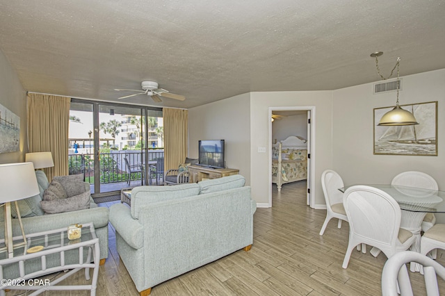 living room featuring ceiling fan, a wall of windows, light hardwood / wood-style floors, and a textured ceiling