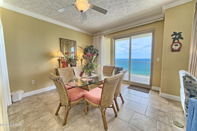 dining area featuring a water view, ceiling fan, ornamental molding, and a textured ceiling