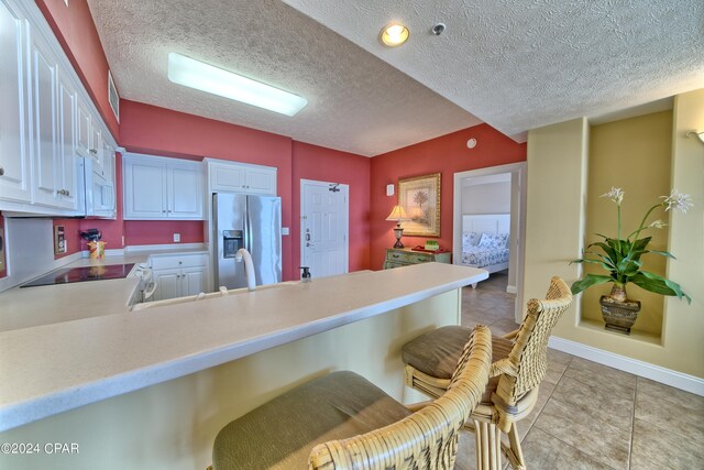 kitchen featuring a breakfast bar, range, white cabinetry, stainless steel fridge with ice dispenser, and kitchen peninsula