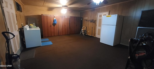 basement featuring wood walls, ceiling fan, white fridge, and washer / dryer