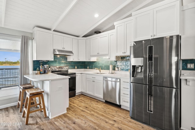 kitchen with backsplash, appliances with stainless steel finishes, light wood-type flooring, lofted ceiling with beams, and a breakfast bar area