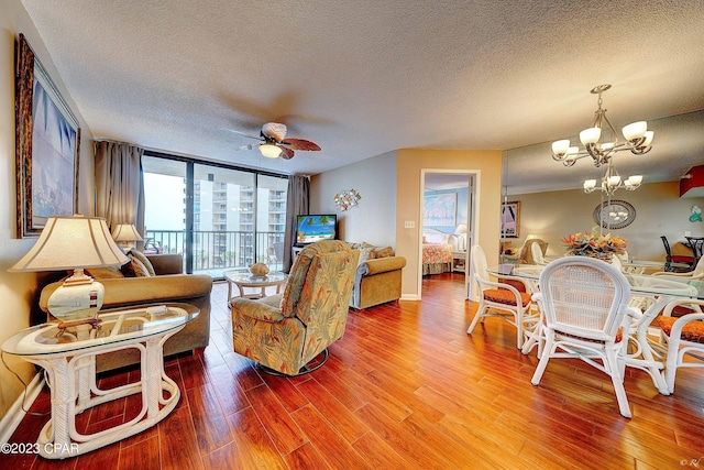 living room featuring hardwood / wood-style flooring, a wall of windows, ceiling fan with notable chandelier, and a textured ceiling