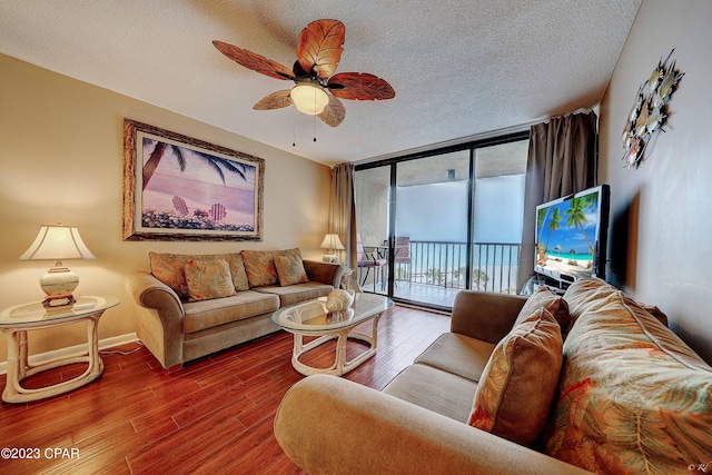 living room with ceiling fan, a textured ceiling, a wall of windows, and wood-type flooring