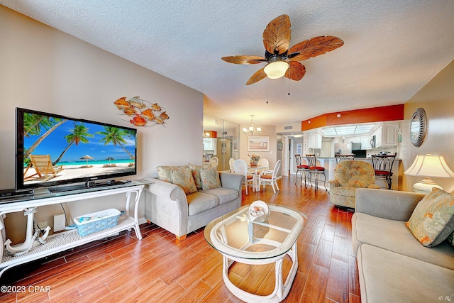 living room with wood-type flooring, ceiling fan with notable chandelier, and a textured ceiling