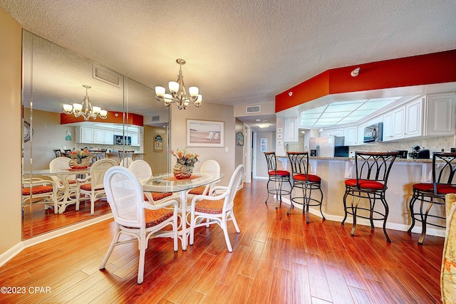 dining area with a textured ceiling, a chandelier, and light hardwood / wood-style floors