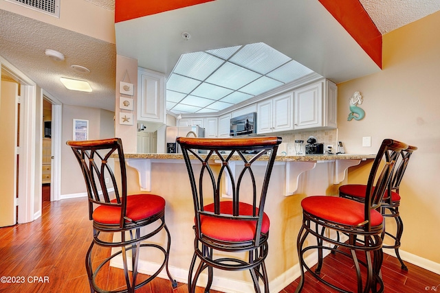 kitchen with white cabinetry, a kitchen breakfast bar, kitchen peninsula, and light wood-type flooring