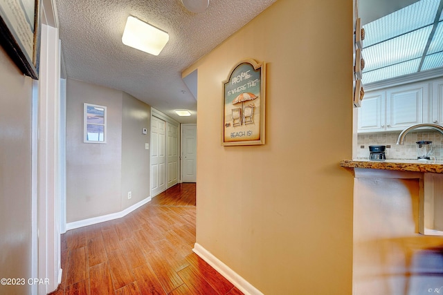 hall with a textured ceiling and light hardwood / wood-style flooring