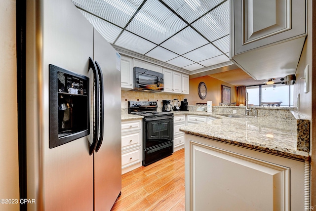 kitchen featuring sink, white cabinetry, kitchen peninsula, light stone countertops, and black appliances