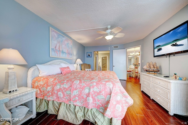 bedroom with dark hardwood / wood-style floors, ceiling fan with notable chandelier, and a textured ceiling