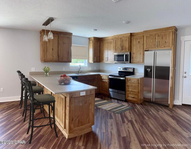 kitchen featuring sink, stainless steel appliances, dark wood-type flooring, kitchen peninsula, and pendant lighting