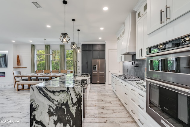 kitchen featuring decorative light fixtures, light wood-type flooring, backsplash, stainless steel appliances, and an island with sink