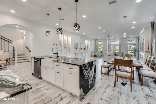 kitchen featuring hanging light fixtures, light hardwood / wood-style flooring, white cabinetry, a center island with sink, and ceiling fan