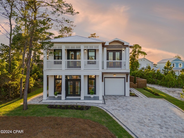 view of front of property featuring french doors, a balcony, a lawn, and a garage