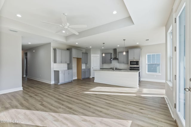 unfurnished living room with ceiling fan, a raised ceiling, and light wood-type flooring