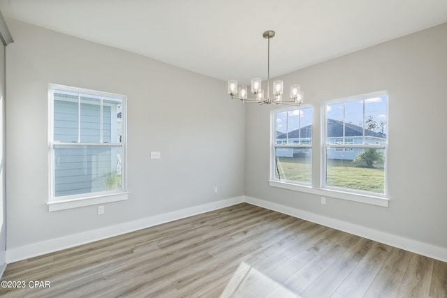 empty room with light hardwood / wood-style floors and an inviting chandelier