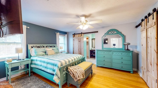 bedroom with a barn door, light hardwood / wood-style flooring, multiple windows, and ceiling fan