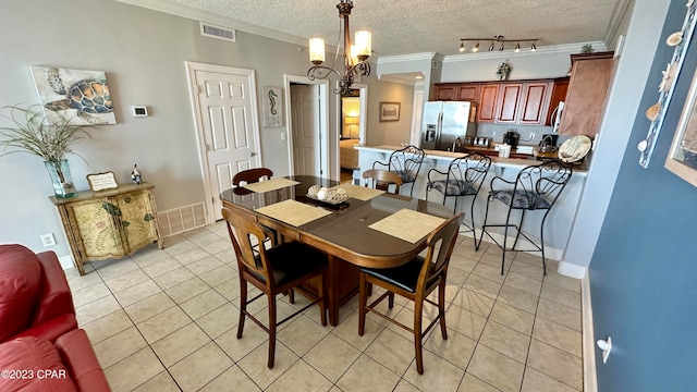 dining room with light tile floors, a textured ceiling, rail lighting, a chandelier, and crown molding