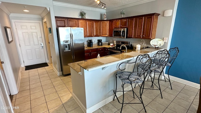 kitchen with stainless steel appliances, a breakfast bar, ornamental molding, track lighting, and light stone counters