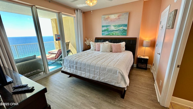 bedroom featuring a water view, multiple windows, access to outside, and light hardwood / wood-style flooring