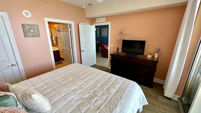 bedroom featuring hardwood / wood-style floors, a textured ceiling, vaulted ceiling, and ensuite bathroom