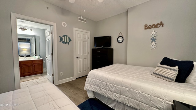 bedroom with ensuite bath, light hardwood / wood-style floors, a textured ceiling, and ceiling fan