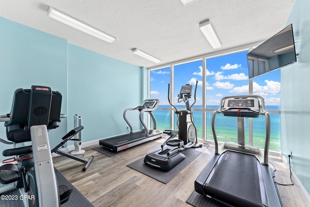 gym with a textured ceiling, a wall of windows, a water view, and light hardwood / wood-style flooring