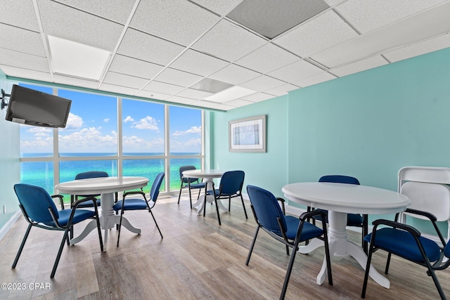 dining room featuring floor to ceiling windows, light hardwood / wood-style floors, a drop ceiling, and a water view