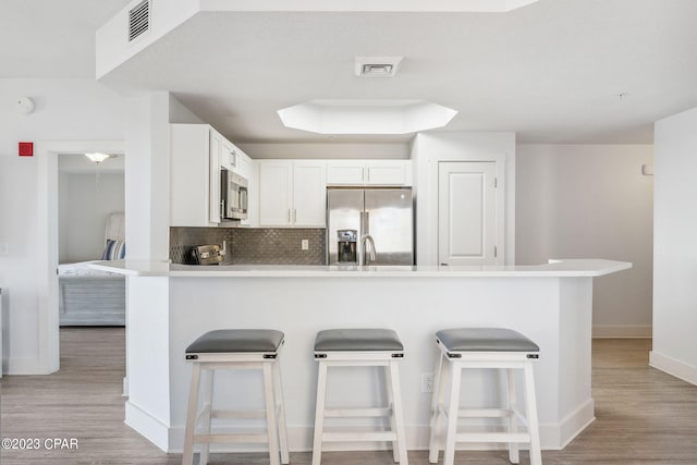 kitchen featuring light hardwood / wood-style floors, a breakfast bar, appliances with stainless steel finishes, white cabinets, and backsplash