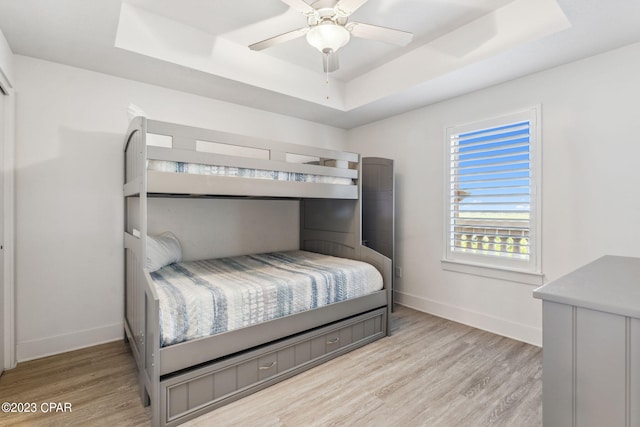 bedroom with ceiling fan, a raised ceiling, and light hardwood / wood-style flooring