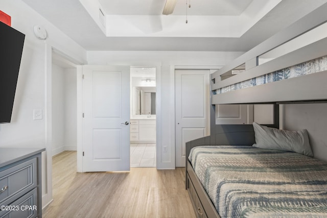 bedroom featuring ceiling fan, connected bathroom, light hardwood / wood-style flooring, and a raised ceiling