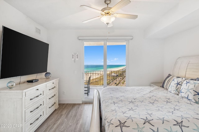 bedroom featuring a water view, multiple windows, access to exterior, and light wood-type flooring