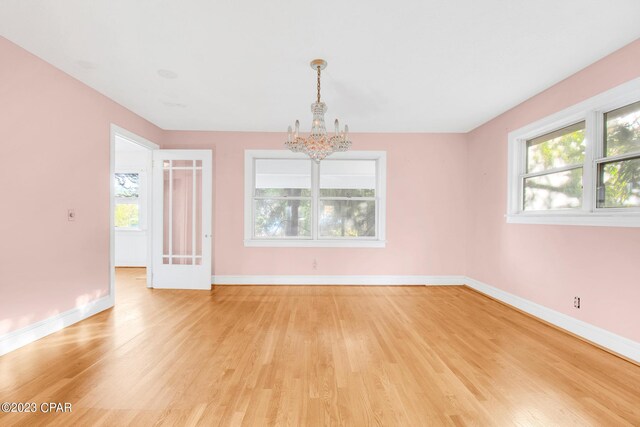 spare room with a healthy amount of sunlight, a notable chandelier, and light hardwood / wood-style flooring