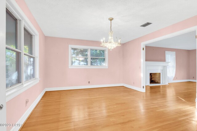 unfurnished living room with an inviting chandelier, plenty of natural light, and light hardwood / wood-style floors