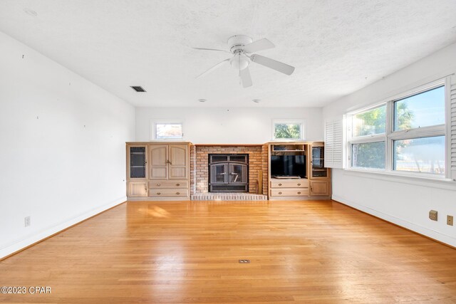 unfurnished living room featuring a brick fireplace, light hardwood / wood-style flooring, and a textured ceiling