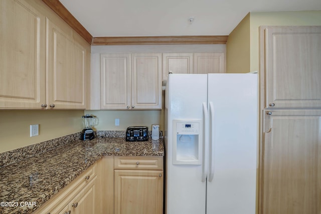 kitchen featuring dark stone counters, white fridge with ice dispenser, and light brown cabinetry