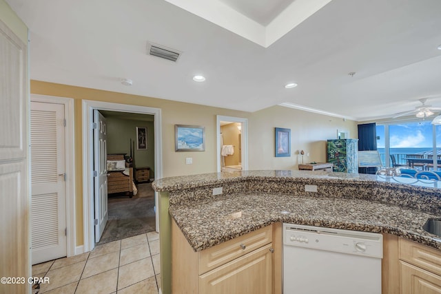 kitchen with ceiling fan, light tile patterned floors, dark stone countertops, dishwasher, and light brown cabinetry