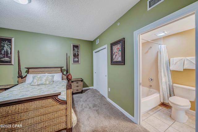 bedroom with a textured ceiling, a closet, connected bathroom, and carpet flooring