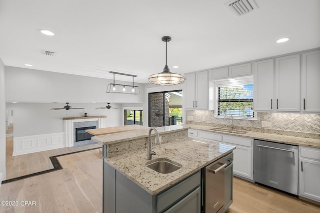 kitchen featuring dishwasher, pendant lighting, a center island with sink, and sink