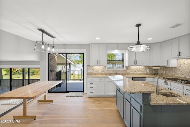 kitchen featuring decorative light fixtures, light stone counters, tasteful backsplash, and sink