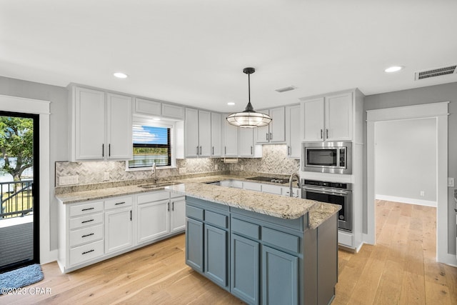 kitchen with light stone countertops, sink, stainless steel appliances, decorative light fixtures, and a kitchen island