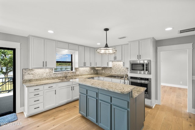 kitchen featuring appliances with stainless steel finishes, sink, pendant lighting, light hardwood / wood-style floors, and a kitchen island